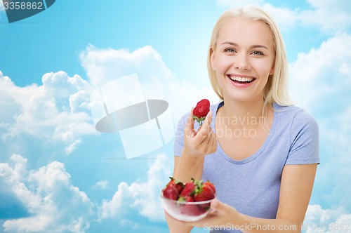 Image of happy woman eating strawberry over sky