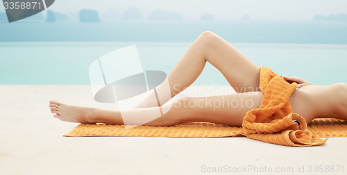 Image of close up of woman legs with orange towel on beach