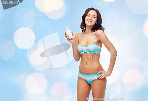 Image of happy young woman in swimsuit holding sunscreen