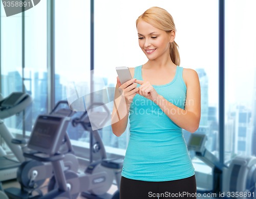 Image of smiling sporty woman with smartphone in gym