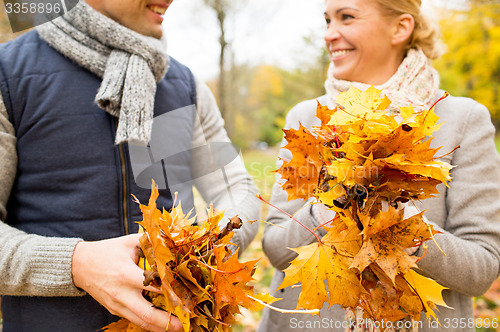 Image of smiling couple with maple leaves in autumn park