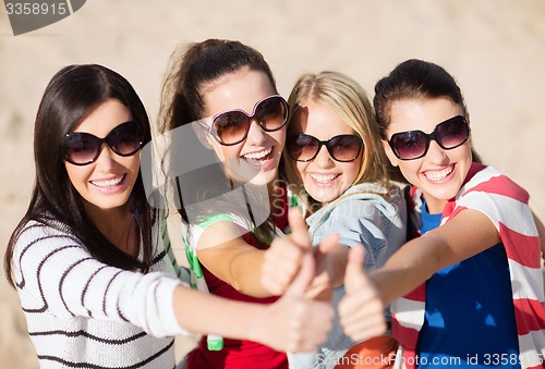 Image of happy teenage girls showing thumbs up on beach