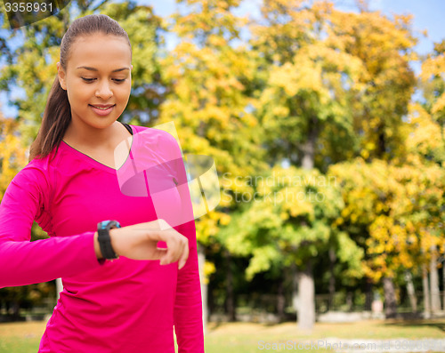 Image of smiling woman with heart rate watch at autumn park