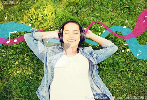 Image of smiling young girl in headphones lying on grass