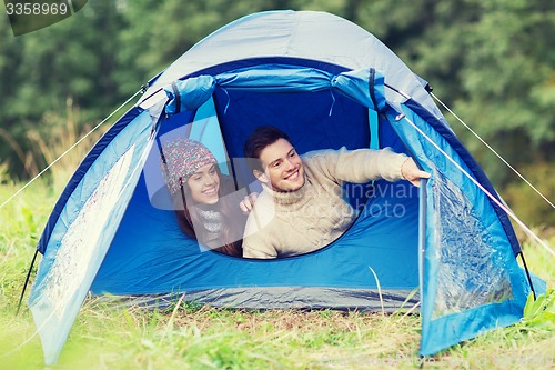 Image of smiling couple of tourists looking out from tent