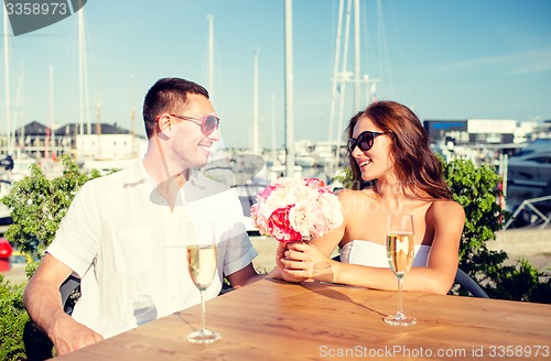 Image of smiling couple with bunch and champagne at cafe