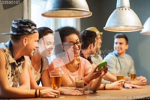 Image of happy friends with smartphone and drinks at bar