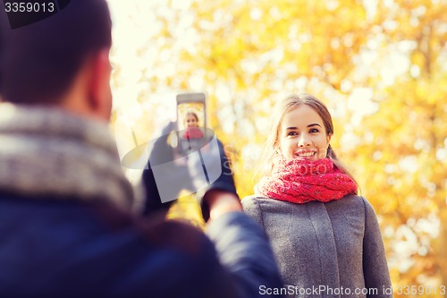 Image of smiling couple with smartphone in autumn park