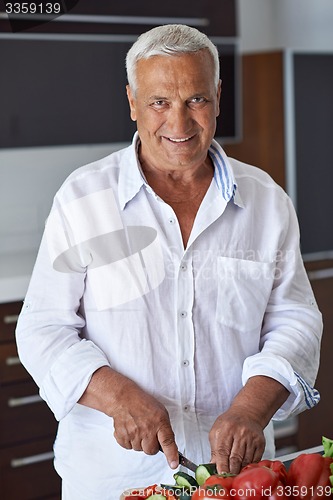 Image of senior man cooking at home preparing salad in kitchen