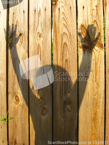 Image of shadows of teen's hand raising up on the fence