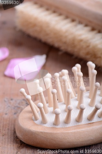 Image of hair brush, rose flower petals, comb on wooden plate. close up