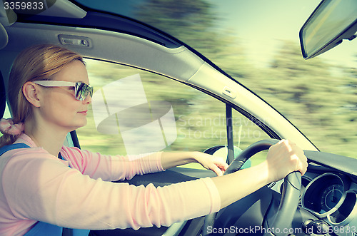 Image of Pretty woman in sunglasses driving fast car filtered and toned