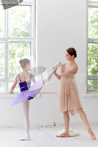 Image of The little ballerina posing at ballet barre with personal teacher in dance studio