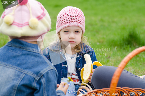 Image of The sad girl at a picnic eats banana