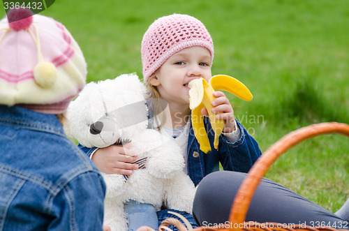 Image of Girl on picnic eats a banana and holds bear