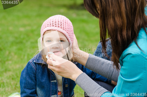 Image of Mother wipes his mouth with a napkin girl on picnic