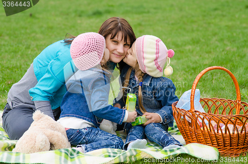 Image of Two daughters kissing mother while on a picnic