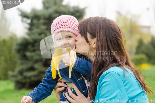 Image of Mom kisses the girl who eats a banana on picnic