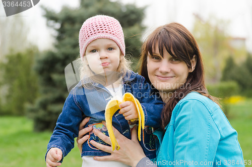 Image of Mom keeps girl who eats a banana on picnic