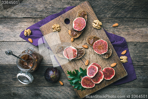 Image of Cut figs, nuts and bread with jam on wooden choppingboard