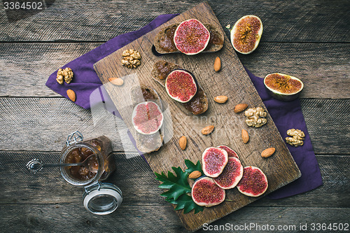Image of Sliced figs, nuts and bread with jam on choppingboard in rustic 