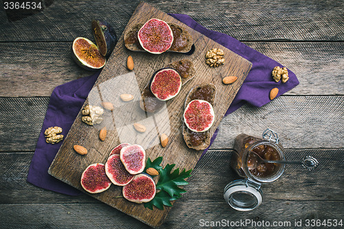 Image of Cut figs, nuts and bread with jam on choppingboard in rustic sty