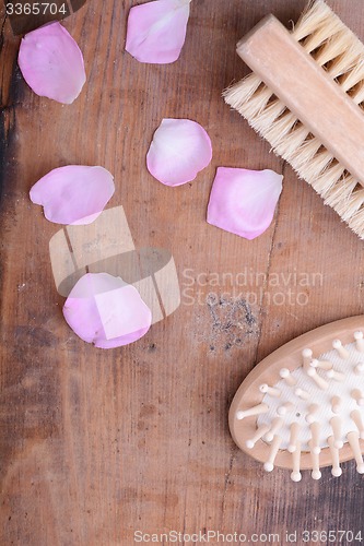 Image of hair brush, rose flower petals, comb on wooden plate