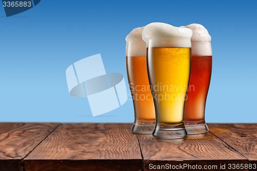 Image of Different beer in glasses on wooden table and blue background