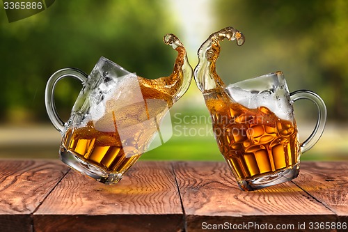 Image of Splash of beer in two glasses on wooden table against park