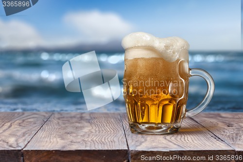 Image of Glass of beer on wooden table with sea on background