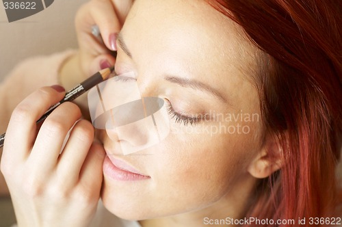 Image of beautician is doing make-up to red-haired woman