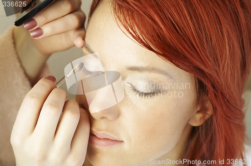 Image of beautician is doing make-up to red-haired woman