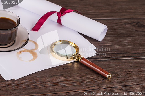 Image of Coffee cup, paper sheets and detective magnifying glass