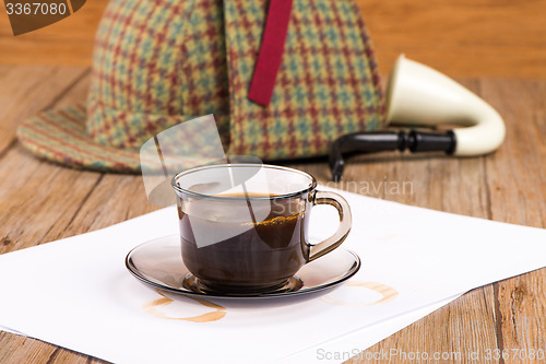 Image of Coffee cup, paper sheets and detective hat