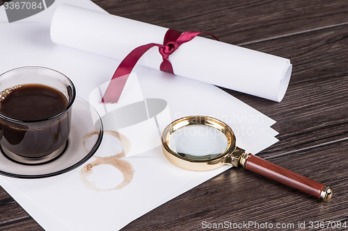 Image of Coffee cup, paper sheets and detective magnifying glass
