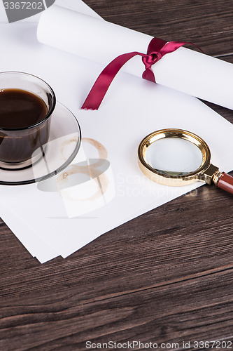 Image of Coffee cup, paper sheets and detective magnifying glass