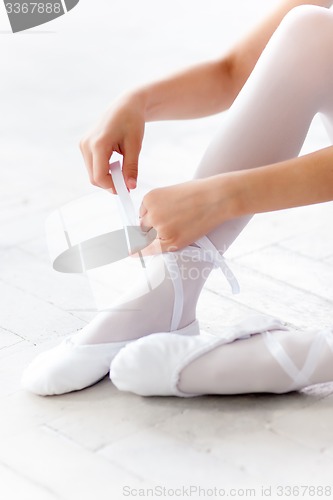 Image of little ballerina puting on foot pointe shoes