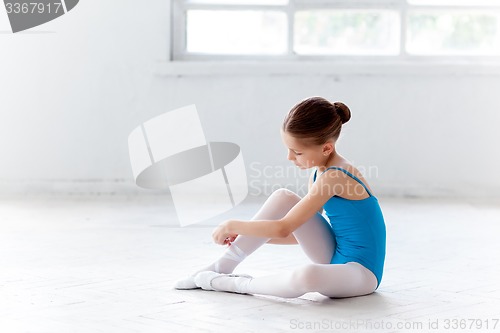 Image of Beautiful little ballerina in blue dress for dancing puting on foot pointe shoes