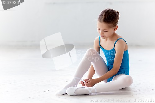 Image of Beautiful little ballerina in blue dress for dancing puting on foot pointe shoes