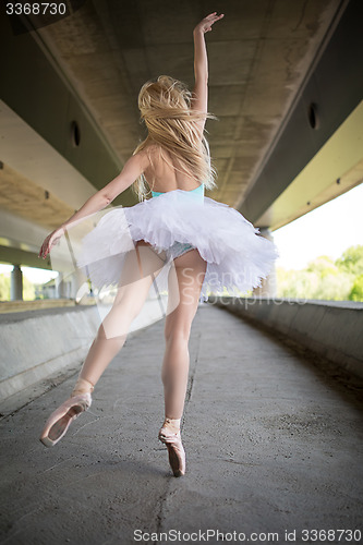 Image of Graceful ballerina doing dance exercises on a concrete bridge 