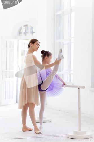 Image of The little ballerina posing at ballet barre with personal teacher in dance studio