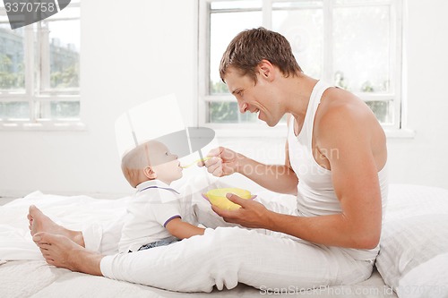 Image of Young father with his nine months old son on the bed at home