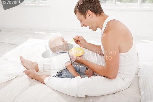 Image of Young father with his nine months old son on the bed at home