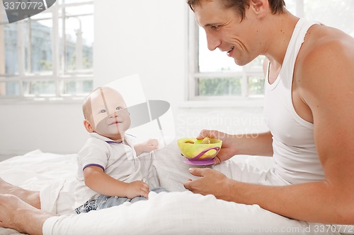 Image of Young father with his nine months old son on the bed at home