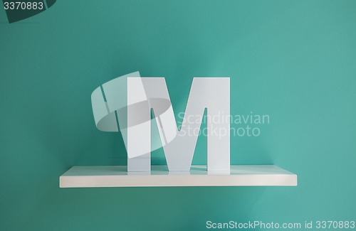 Image of Letter M turquoise color on a white shelf.