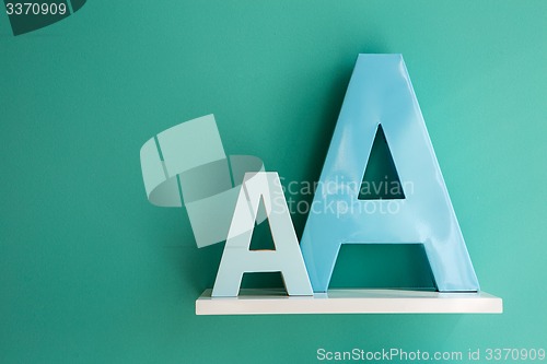 Image of Letters A small and big size turquoise color on a white shelf.