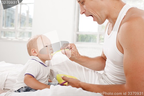 Image of Young father with his nine months old son on the bed at home