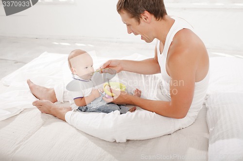 Image of Young father with his nine months old son on the bed at home