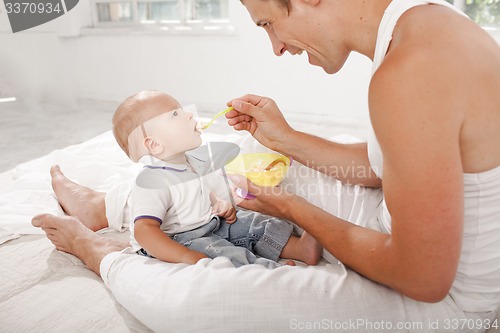 Image of Young father with his nine months old son on the bed at home