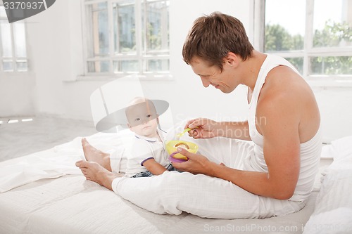 Image of Young father with his nine months old son on the bed at home